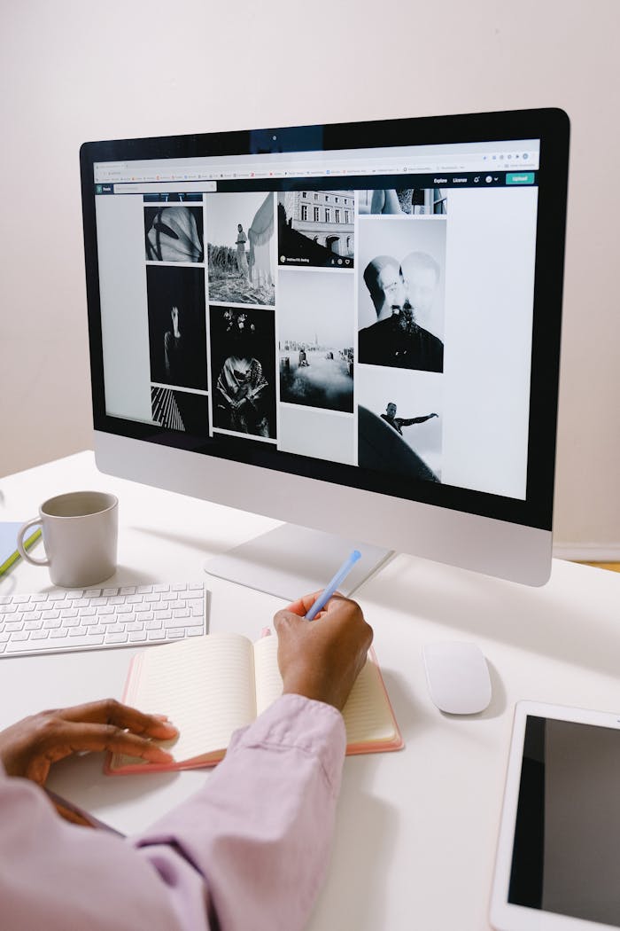 Back view of crop anonymous African American female taking notes in planner and working with computer at table