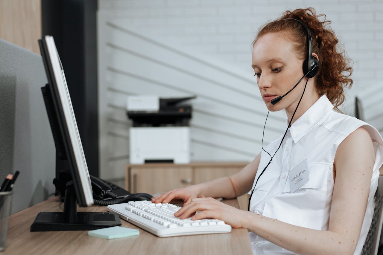A female call center agent typing on a keyboard while wearing a headset at her desk.